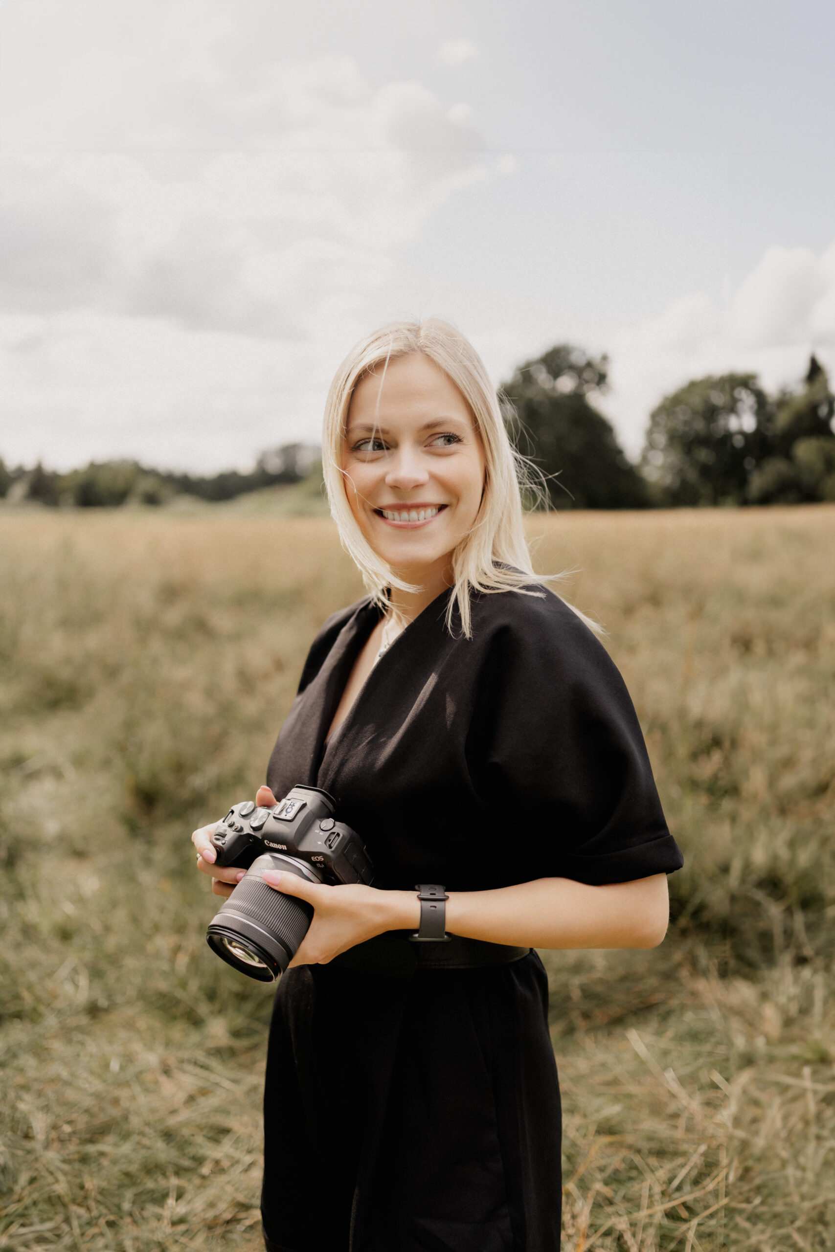 Hochzeitsfotografin Laura steht auf einem Feld mit Kamera in der Hand