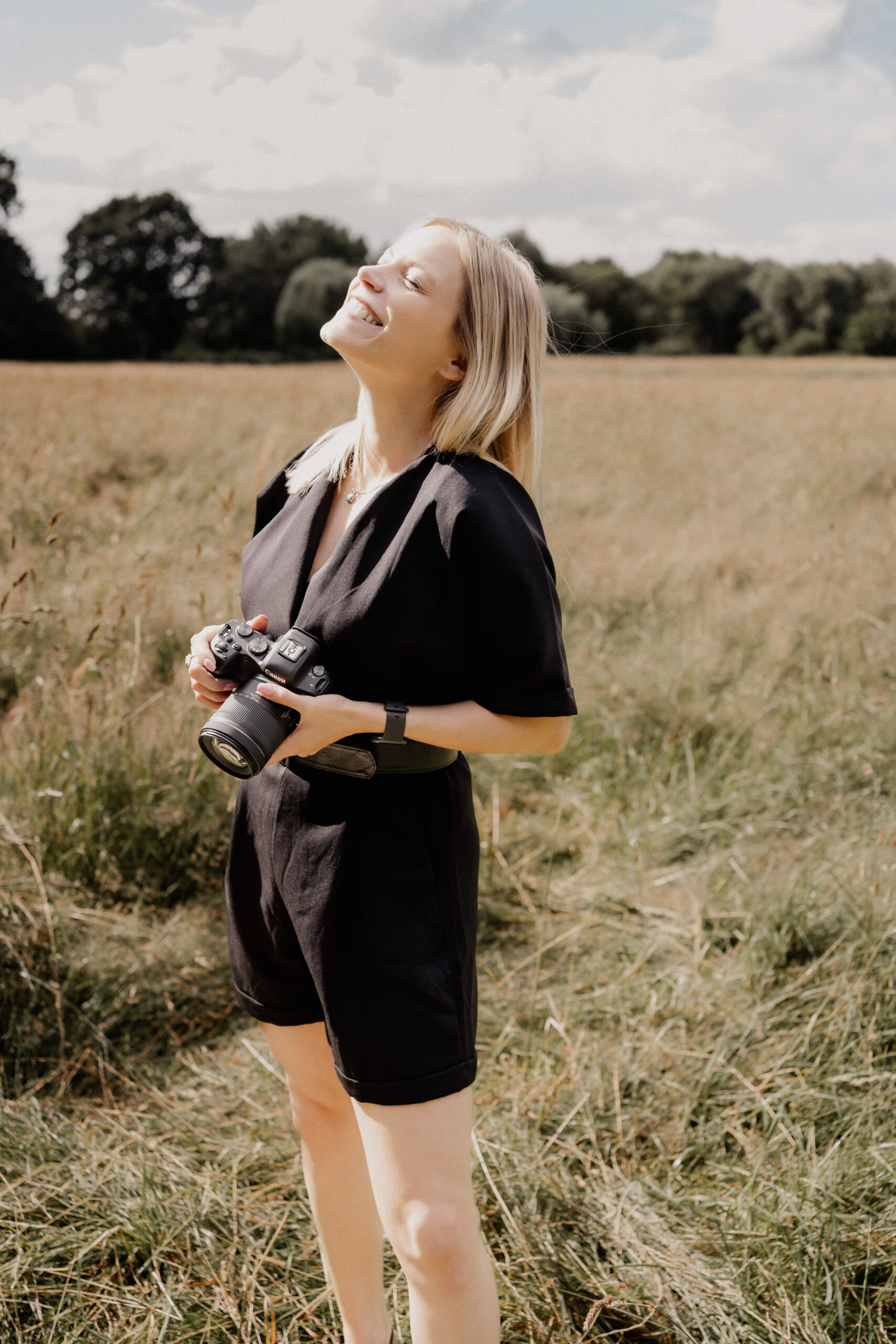 Hochzeitsfotografin Laura steht auf einem Feld mit Kamera in der Hand und schaut nach oben