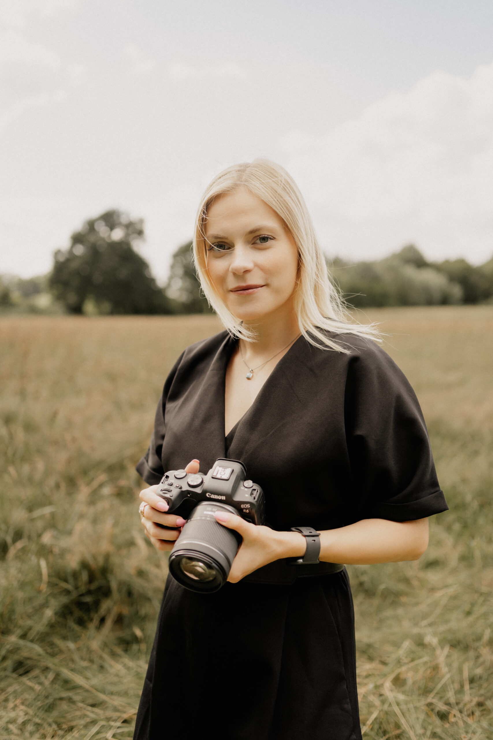 Hochzeitsfotografin Laura steht auf einem Feld mit Kamera in der Hand